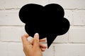 Hand holding an empty black hand-cuted paper speech bubble on white brick wall textured background. .