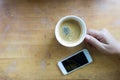 Hand holding espresso coffee in white cup with smart phone and copy space Royalty Free Stock Photo