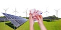 Hand holding euro banknote with photovoltaic panels and wind turbines at the background. Royalty Free Stock Photo