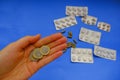 Hand holding euro coin across pills, and capsules on blue background close-up. Finance, healthcare, medicine concept. Pricing, ins