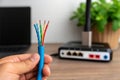Hand holding exposed multicolored wires. Close-up of tech and connectivity. Router with cables in background. Royalty Free Stock Photo