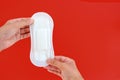 Hand holding feminine sanitary napkin, an absorbent item worn by a woman while menstruating, on red background Royalty Free Stock Photo
