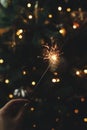 Hand holding firework against christmas tree lights in dark room. Happy New Year! Merry Christmas! Burning sparkler in female hand Royalty Free Stock Photo