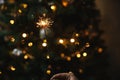 Hand holding firework against christmas tree lights in dark room. Happy New Year! Merry Christmas! Burning sparkler in female hand Royalty Free Stock Photo