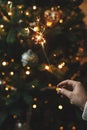 Hand holding firework against christmas tree lights in dark room. Happy New Year! Merry Christmas! Burning sparkler in female hand Royalty Free Stock Photo