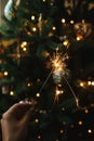 Hand holding firework against christmas tree lights in dark room. Happy New Year! Merry Christmas! Burning sparkler in female hand Royalty Free Stock Photo