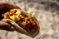 A hand holding a fish taco above a sandy beach Royalty Free Stock Photo