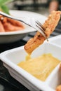 Hand holding folk french fries with in mayonnaise and ketchup sauce in the background. Mayonnaise in small round white ceramic di