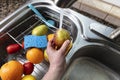 Hand holding fresh pear fruit under running water from kitchen sink faucet. Clean or thoroughly washing concept Royalty Free Stock Photo