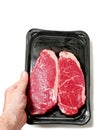 Hand holding fresh strip loin steak on a black plastic tray and on white background. Meat industry product. Top quality meat with