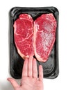 Hand holding fresh strip loin steak on a black plastic tray and on white background. Meat industry product. Top quality meat with