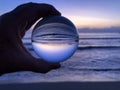 Hand holding glass ball, beach to sea view at dawn