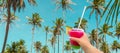 Hand holding a glass with cocktail and straw and Beautiful Palm trees in blue sky background Royalty Free Stock Photo