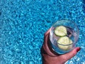 Hand holding a glass of cucumber water poolside