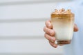 Hand holding a glass of iced Dalgona Coffee on white background