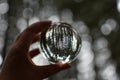 Hand holding a glass photography sphere reflecting trees in the forest on blurry background. Nature mystical concept