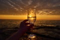 Morning energy. hand holding glass of white wine and with sea and beautiful sunrise at background, close-up. Holiday, day off Royalty Free Stock Photo
