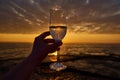 Hand holding glass of white wine and with sea and beautiful sunset at background, close-up. Summer evening relaxed mood concept Royalty Free Stock Photo