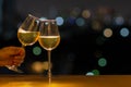 Hand holding a glass of white wine toasting to celebration and party concept put on wooden table of rooftop bar with colorful