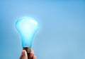 Hand holding glowing blue light bulb on blue background with copy space, symbolizing innovation, smart technology, creativity, AI Royalty Free Stock Photo