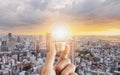 Hand holding glowing light bulb, with city sunrise background Royalty Free Stock Photo