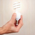 Hand holding a glowing tungsten bulb on light wood background