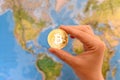 Hand holding gold coin of Bitcoin against map of world. Bitcoin Royalty Free Stock Photo