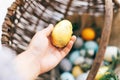 Hand holding golden Easter egg and stylish eggs with green buxus branches in rustic wicker basket on white wooden background. Royalty Free Stock Photo