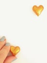 Hand holding a golden heart in the lower left corner and another heart alone in the upper right corner.