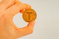 A hand is holding a golden Tether coin with its symbol, against a plain background This image could be used for Royalty Free Stock Photo