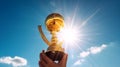 Hand holding golden trophy under the sunlight with blue sky background