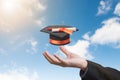 Hand holding graduation hat on blue sky background.