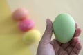 A hand holding a green pastel Easter egg with colorful background Royalty Free Stock Photo