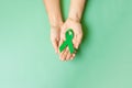 Hand holding green Ribbon for supporting people living and illness. Liver, Gallbladders bile duct, kidney Cancer and Lymphoma