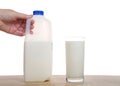 Hand holding half gallon of milk next to full glass of milk on wooden table