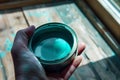 hand holding a halfopen teal paint can lid, light reflecting