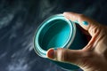 hand holding a halfopen teal paint can lid, light reflecting