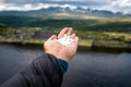 Hand holding a handful of white pills outdoors towards beautiful mountain scenery.