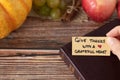 Hand holding a handwritten thanksgiving note to give thanks with grateful heart with Holy Bible and autumn fruit