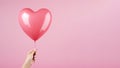 Hand holding heart shaped balloon on blank pink background, advertising shot