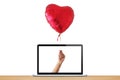 A hand holding a heart-shaped red glossy balloon coming out of the laptop screen Royalty Free Stock Photo