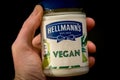 Hand holding Hellmann`s Vegan and plant-based mayonnaise spread on black background.