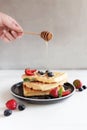 Hand holding honey spoon over stack of waffles with stream on a plate on table