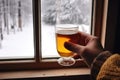 a hand holding a hot toddy against a snowy window