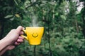 Hand holding hot yellow coffee cup with hand drawn smile face on