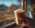 Hand Holding Iced Coffee by Window on Rainy Autumn Day Royalty Free Stock Photo