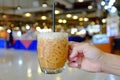 Hand holding iced Thai milk tea glass cup against blur image of department store background Royalty Free Stock Photo
