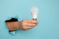 Hand holding an incandescent led light bulb from a torn hole in blue paper Royalty Free Stock Photo