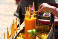 Hand holding incense sticks, lighting from the burning yellow candle. Traditional Thailand buddhist concept