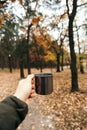 Hand holding an iron cup with a hot drink on a background of autumn forest. vertical photo. mood of adventure and comfort